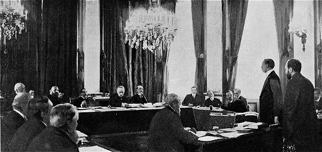 Admirals and lawyers seated at tables in a chandeliered room in Paris, a witness standing