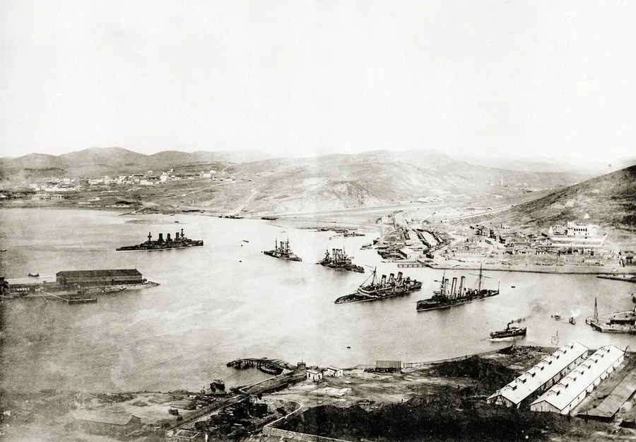 Port Arthur harbour seen from a hill, wrecked battleships lying in the basin below the town