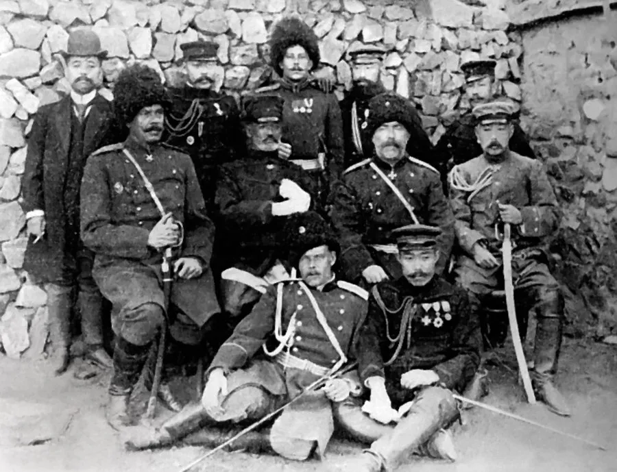 Russian officers in fur caps and Japanese officers in peaked caps posed together before a stone wall