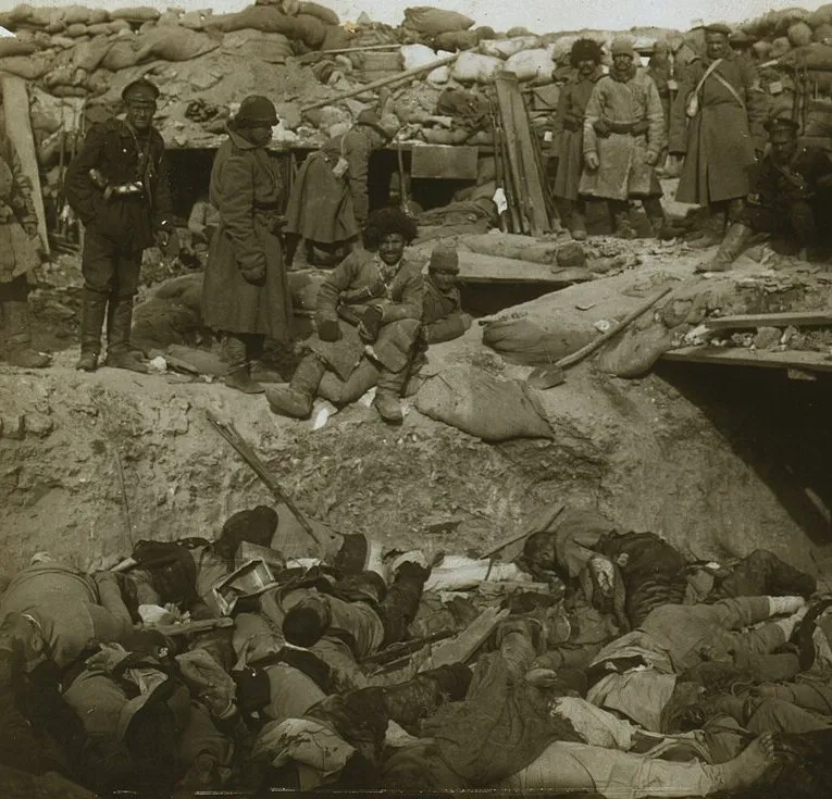 Russian soldiers in fur caps standing behind sandbags above a trench filled with bodies