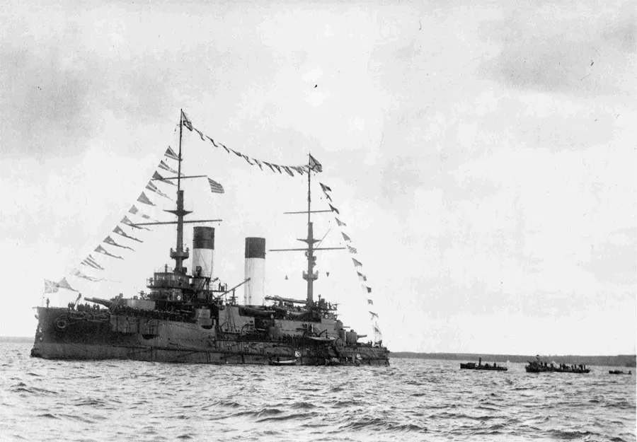 The Russian battleship Knyaz Suvorov at anchor, dressed with flags, small boats beside her